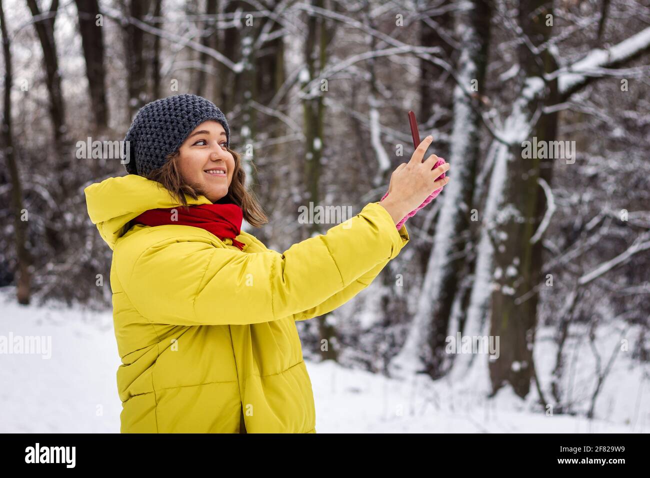 Junge Frau im Wintermantel nimmt Selfie mit dem Smartphone während des Spaziergangs im Freien. Lächelnde kaukasische Frau, die ein Mobiltelefon für Fotonachrichten verwendet Stockfoto