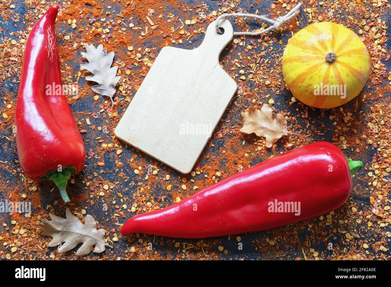 Herbstkonzept. Rote Paprika, Kürbis, Herbstblätter und verstreute zerkleinerte Paprika Stockfoto