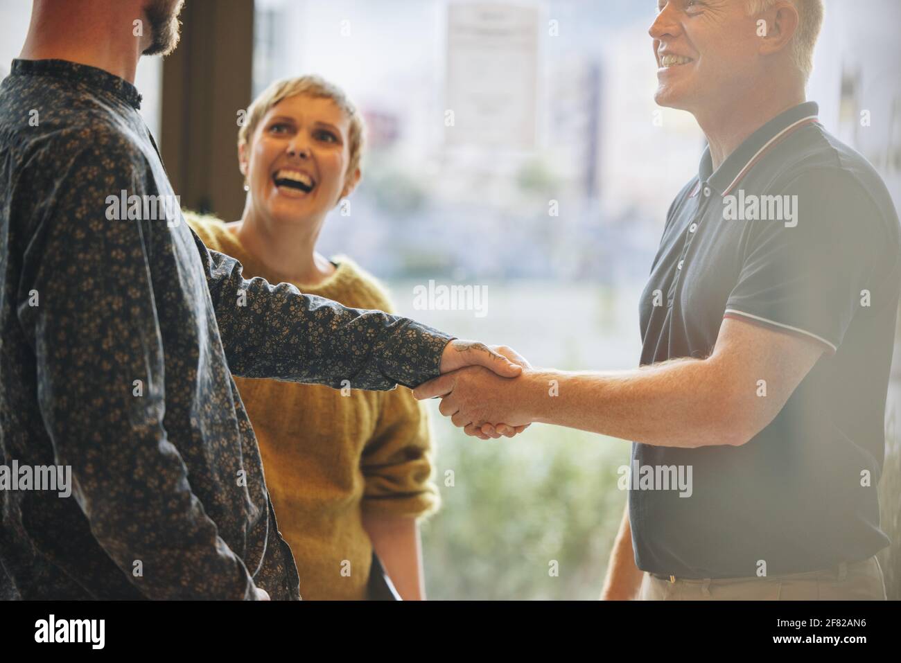 Zwei Geschäftsmänner schütteln die Hand nach einem Deal mit lächelnder Kollegin. Geschäftsleute schütteln nach einem Deal Hand. Stockfoto