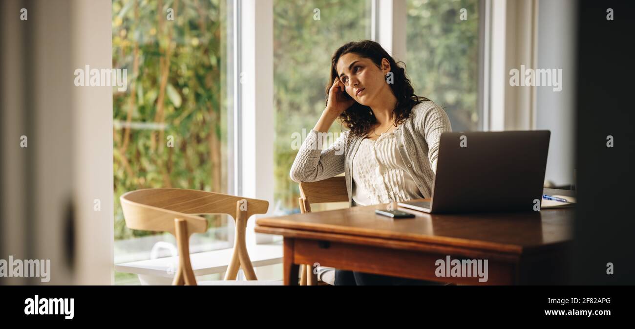 Frau verlor sich bei der Arbeit an einem Laptop tief in Gedanken. Frau besorgt über den Aufenthalt zu Hause und nicht in der Lage zu arbeiten. Stockfoto