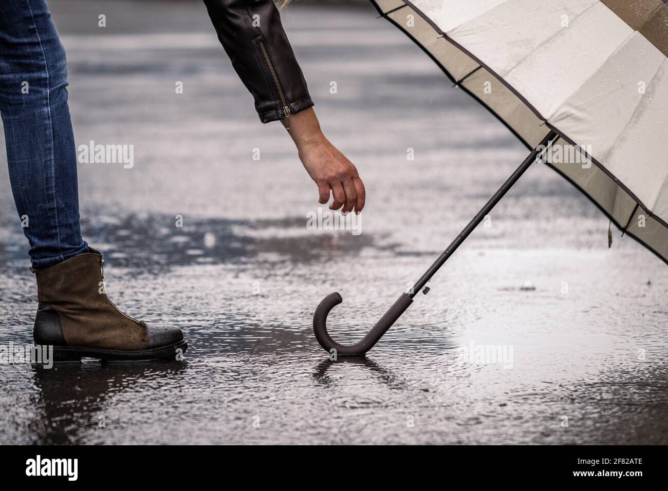 Frau, die bei Regen Regenschirm von der Pfütze auf der Straße abholt. Wind- und Regenwetter in der Stadt Stockfoto