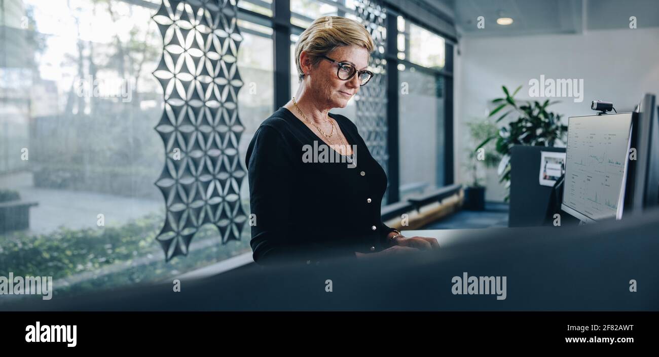 Leitende Geschäftsfrau, die im Büro am Computer arbeitet. Weibliche Führungskraft, die am Stehtisch im modernen Büro arbeitet. Stockfoto
