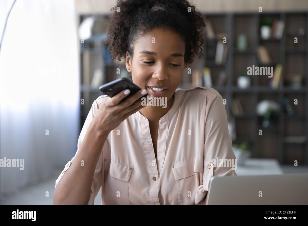 Lächelnde Birazialfrau zeichnet Nachricht auf Handy auf Stockfoto