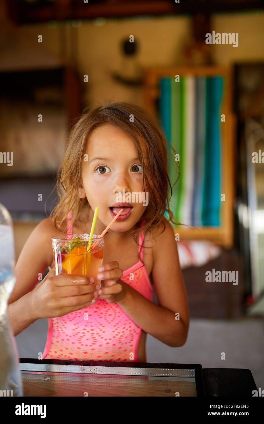 Kleines Mädchen, das sich entspannt und einen Saft in einem tropischen Urlaubsresort mit der Familie genießt Stockfoto