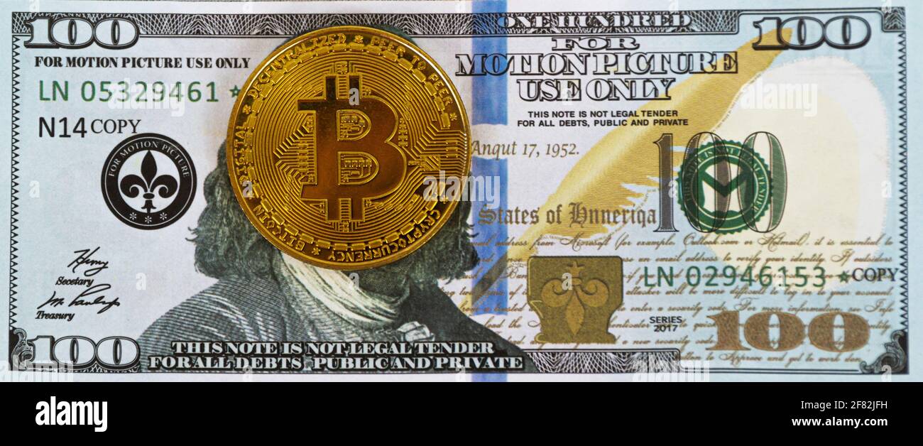 Eine Bitcoin-Goldmünze, die auf einem 100-Dollar-Schein auf dem Gesicht platziert wird. Stockfoto