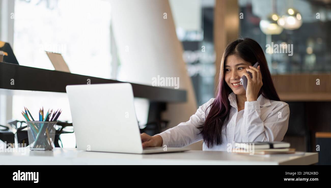 Junge asiatische Geschäftsfrau schön charmant lächelnd und im Gespräch auf die Mobiltelefon während des Tippens auf dem Laptop im Büro Stockfoto