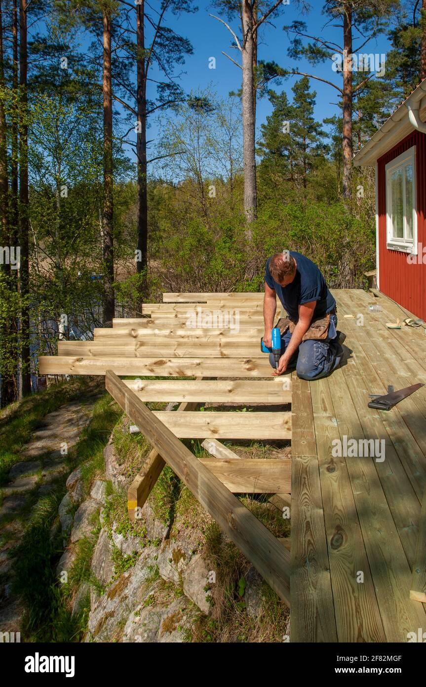 Ein Mann mit Schraubendreher, der Planken auf einem Holzdeck befestigt Stockfoto