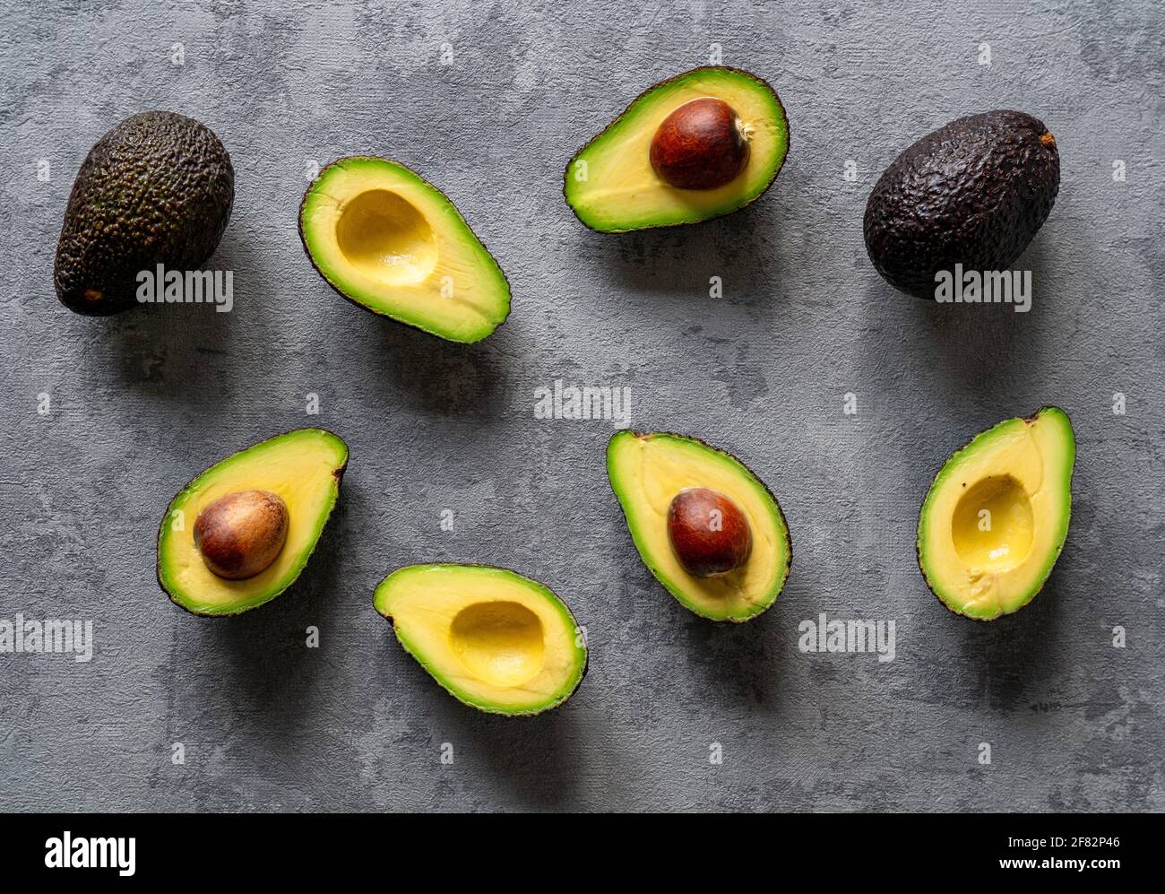 Eine kreative Draufsicht auf geschnittene und ganze Avocados Ein grauer Hintergrund Stockfoto