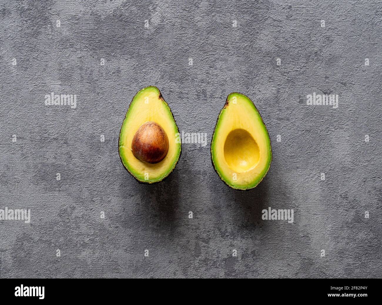 Eine kreative Draufsicht auf eine geschnittene Avocado auf texturierter Oberfläche Grauer Hintergrund Stockfoto