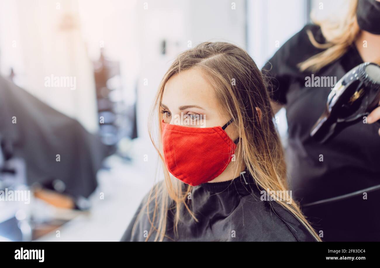 Frau trägt rote Gesichtsmaske immer frisches Styling bei einem Friseur Stockfoto