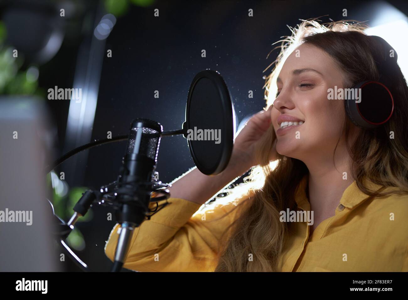 Nahaufnahme Porträt von jungen schönen Frau in gelbem Hemd singen mit Kopfhörer in schwarz modernes Mikrofon. Konzept der Prozess-Aufnahme Song im professionellen Studio. Stockfoto