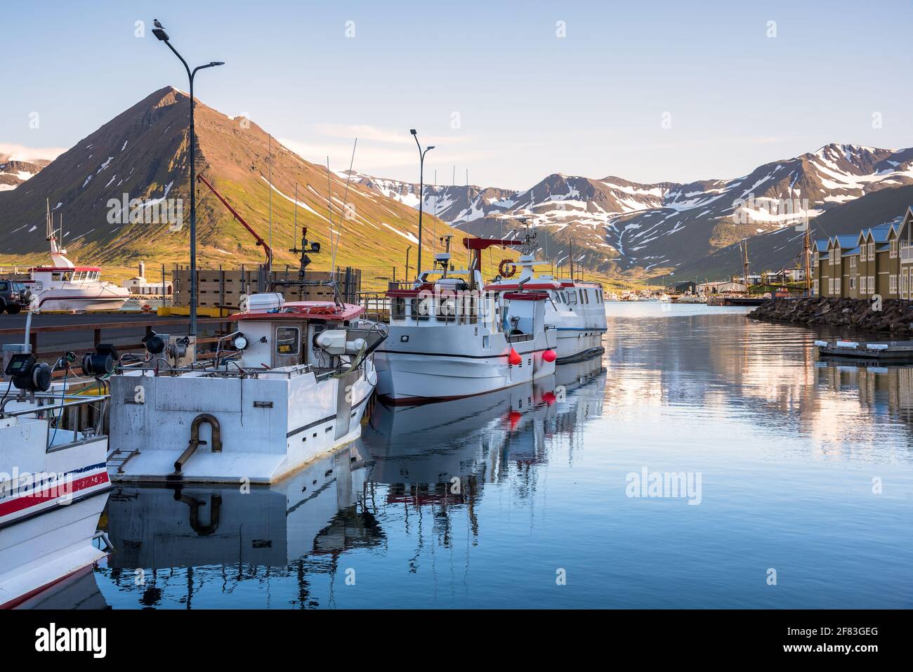 An einem sonnigen Sommertag werden Fischerboote in einem Hafen in einem Fjord an einen Pier gebunden. Majestätische Küstenberge sind im Hintergrund. Stockfoto