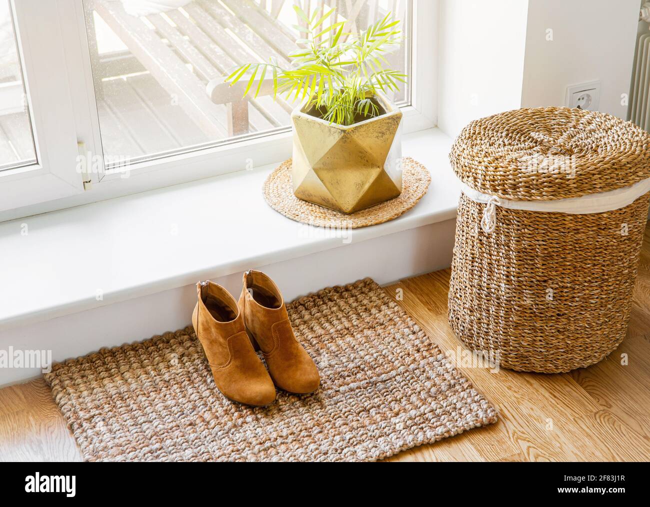 Hartholzboden mit Jute-Fußmatte, Schuhen und Blumentopf und Seegraswaschkorb am Fenster. Natürliche materielle Objekte im Heimkonzept. Inneneinrichtung. Stockfoto