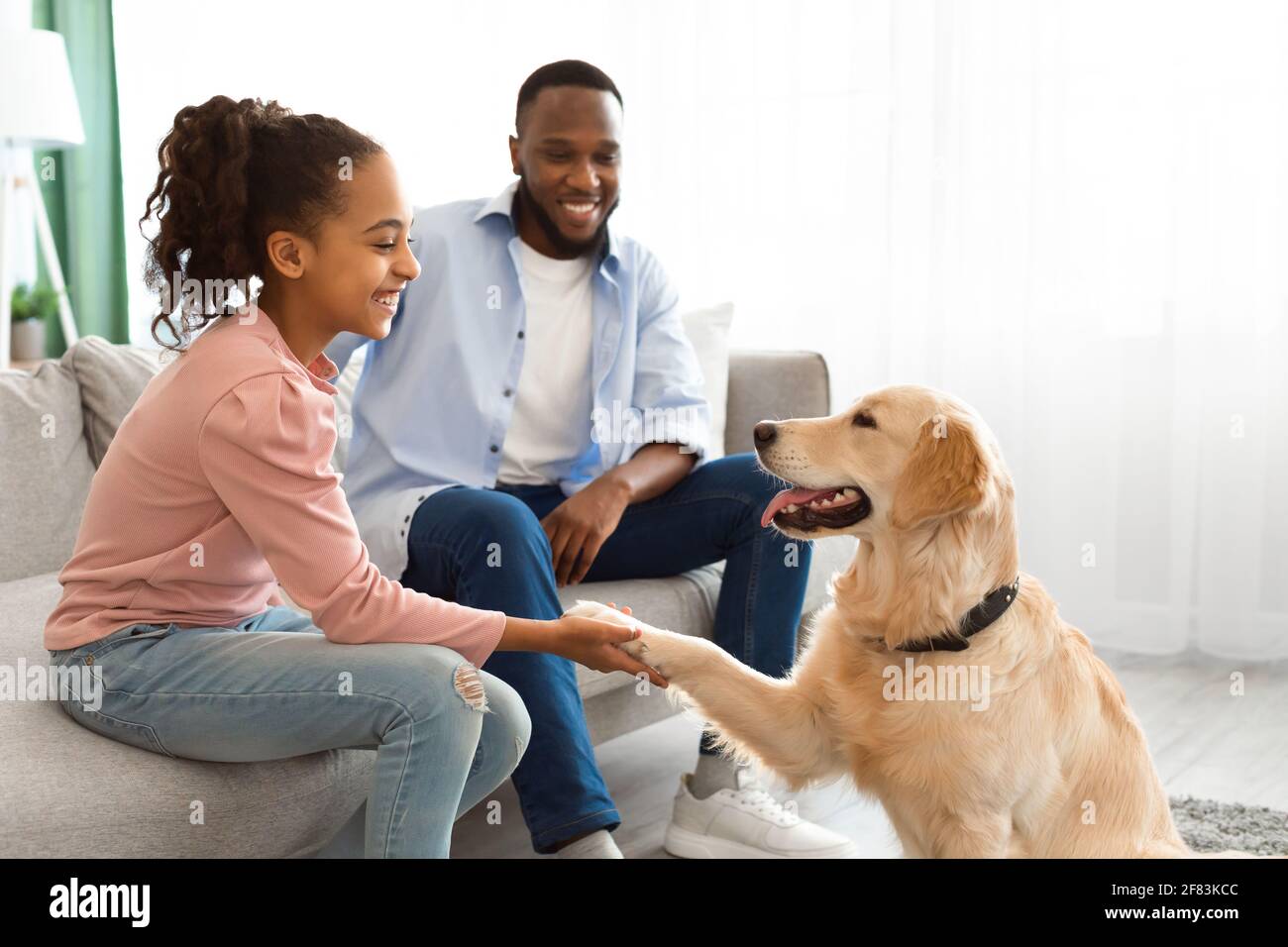 Lächelndes schwarzes Mädchen, das im Wohnzimmer mit Hund spielt Stockfoto