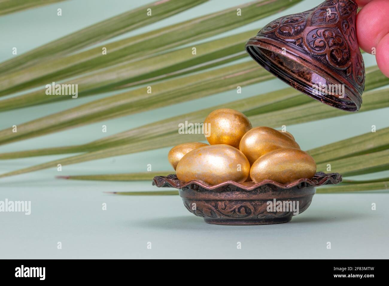 Religiöses islamisches Fest und heiliger Monat des Ramadan, EID KAREEM, Konzept: Eine braune metallische und verzierte Schale mit goldenen Mandel-Süßigkeiten. Palmblätter Stockfoto