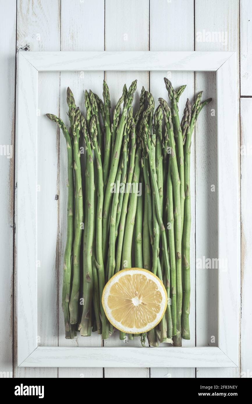 Der Spargel im Rahmen auf dem weißen alten Holzbrett Mit halber Zitrone Stockfoto
