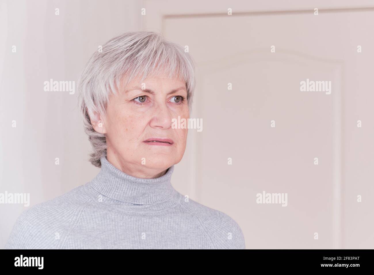 Ein Nahaufnahme-Porträt einer besorgt über etwas ältere kaukasische Frau mit kurzen grauen Haaren in einem grauen Rollkragen. Stockfoto