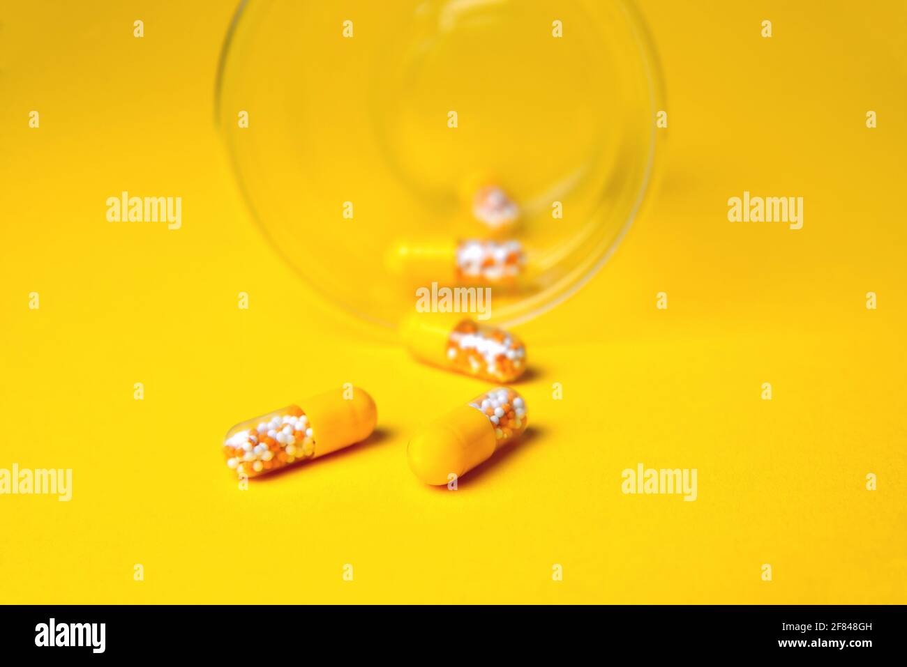 Kapseln in einem Glasbecher. Medizinische Tabletten, Vitamine in einem Granulat, in gelben Kapseln auf einem gelben Hintergrund. Blur als kreative Idee des Autors, Stockfoto