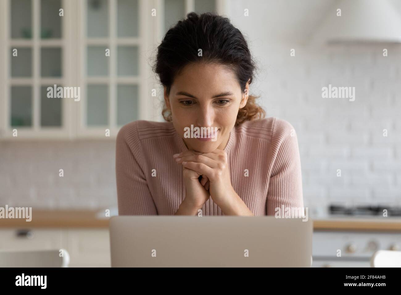 Nachdenkliche lateinische Dame sitzen in der Küche Blick auf Laptop-Bildschirm Stockfoto