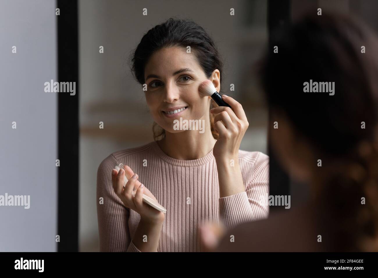 Hübsche Latina Frau stehen in der Nähe des Spiegels Tragen Sie Puder auf das Gesicht auf Stockfoto