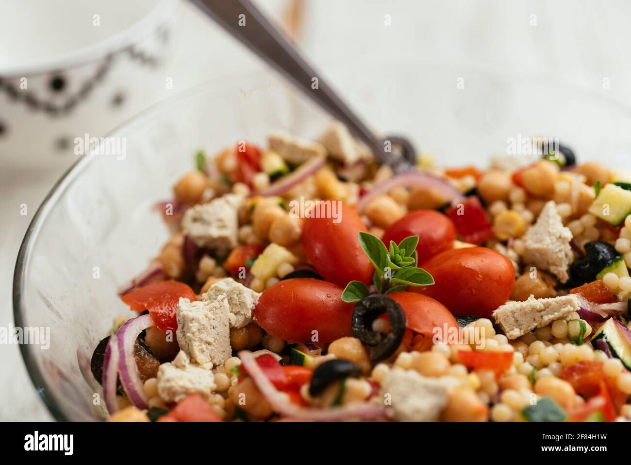 Hausgemachter mediterraner Couscous-Salat mit Paprika, Zucchini, Tomaten, Kichererbsen, olivem und veganem Feta. Stockfoto