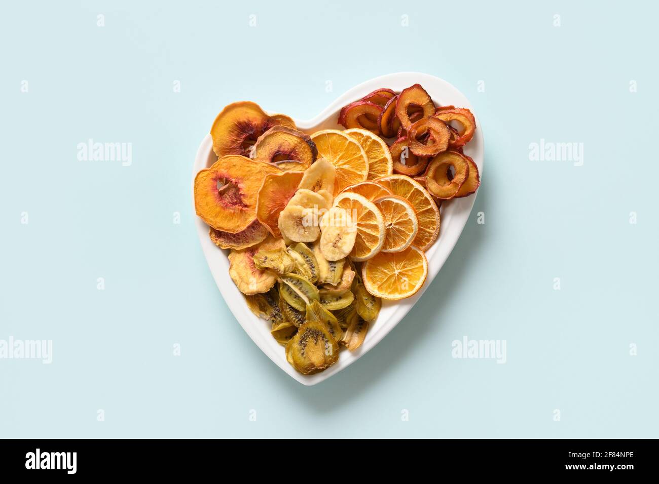 Getrocknete, geschnittene Pflaumen, Kiwi, Pfirsich-Früchte-Chips in Form eines Herztellers auf blauem Hintergrund, Heimtrocknung. Snack vegan frei von Zucker. Blick von oben. Stockfoto