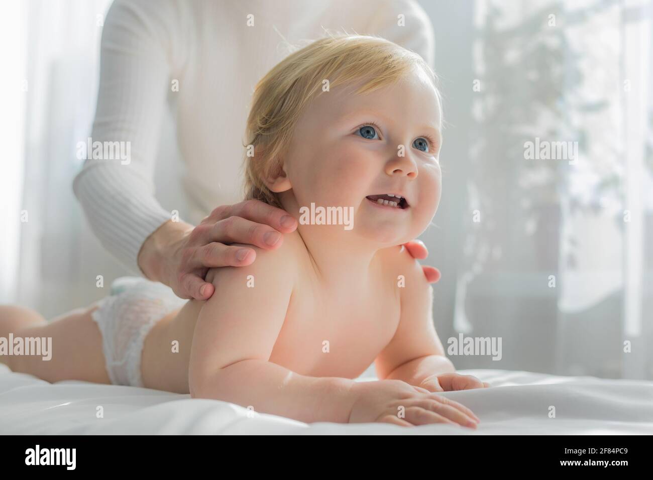 Mama gibt ihrem Baby eine Schulter- und Rückenmassage. Nahaufnahme. Ein zufriedenes Baby liegt auf dem Massagetisch. Stockfoto