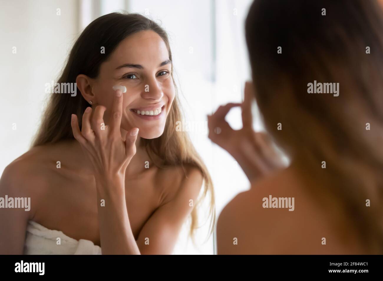 Lächelnde lateinische Frau Creme auf die Gesichtshaut auftragen Stockfoto