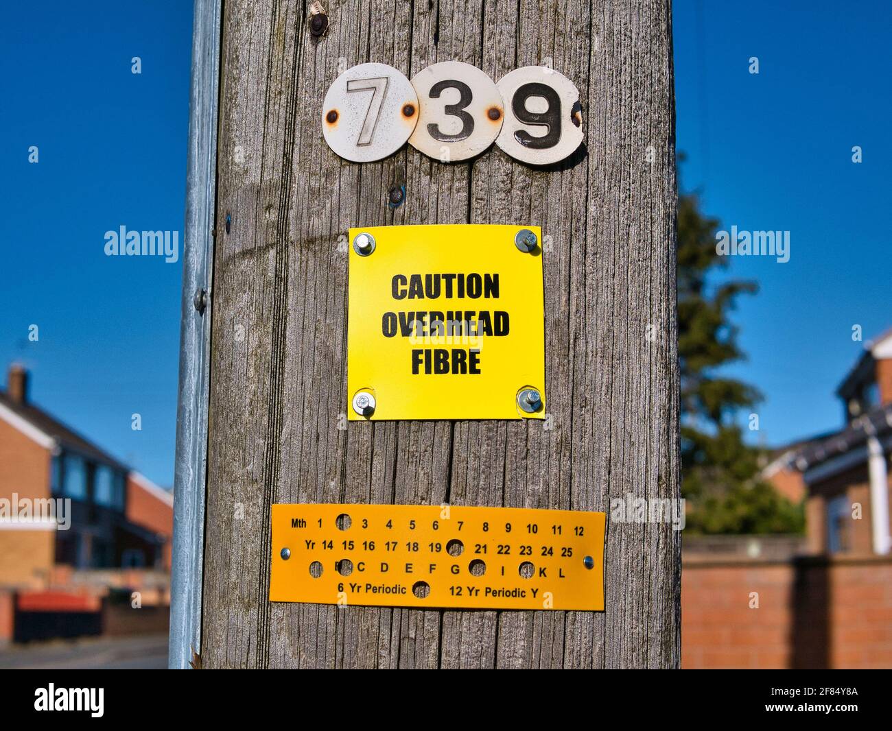Ein gelbes Schild, das an einem hölzernen Telegrafenmast befestigt ist, warnt davor, dass Glasfaserleitungen über dem Kopf liegen. Aufgenommen an einem sonnigen Tag in einem städtischen Gebiet im Nordwesten Englands. Stockfoto