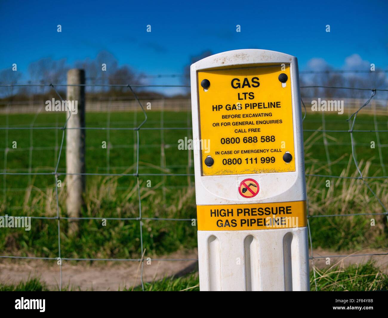 Ein gelbes Warnzeichen, das auf eine Hochdruck-Gasleitung (HP) über Felder in einem ländlichen Gebiet im Nordwesten Großbritanniens hinweist. Stockfoto