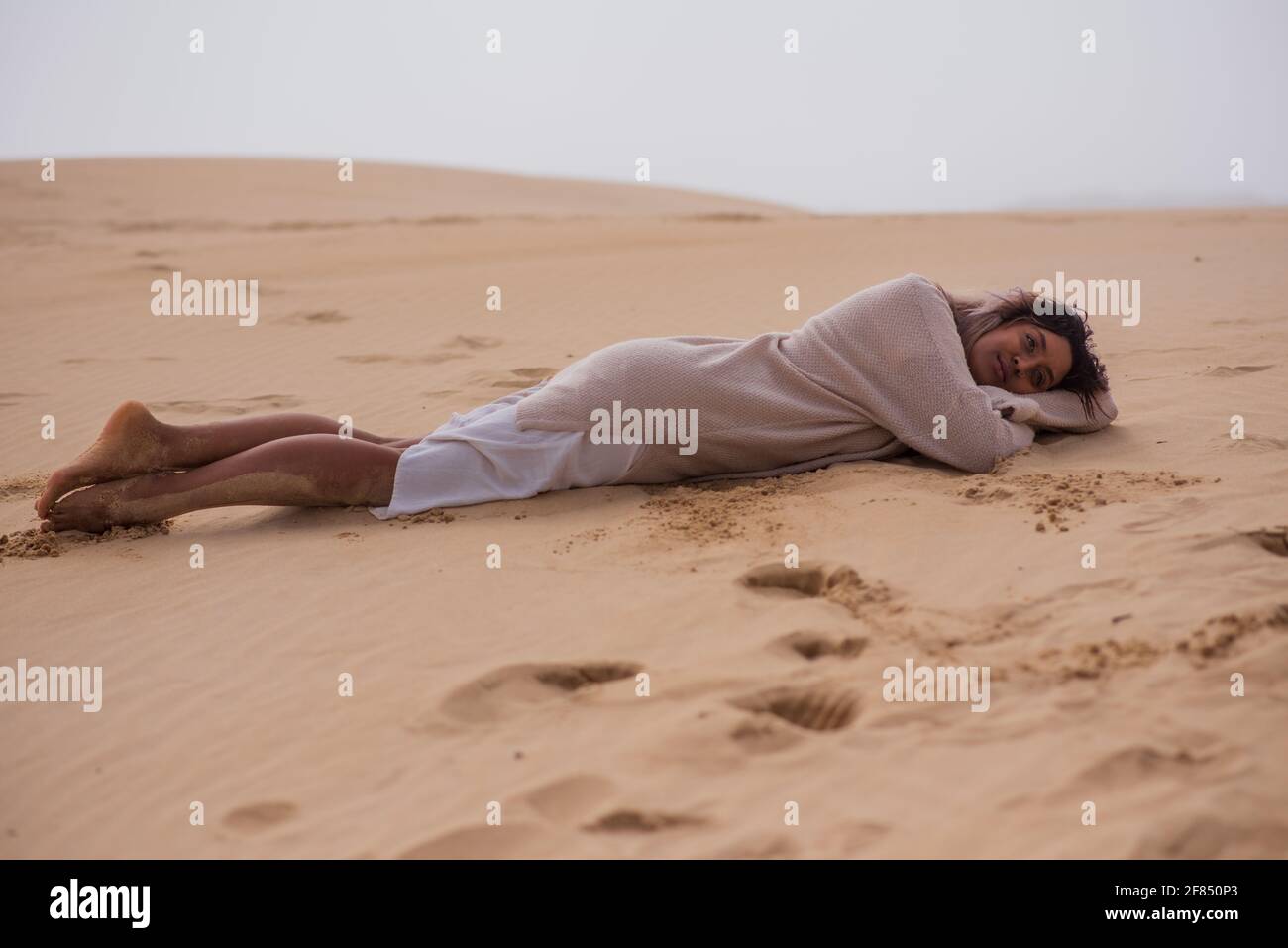 Junge Frau, die am Strand auf Sand liegt Stockfoto