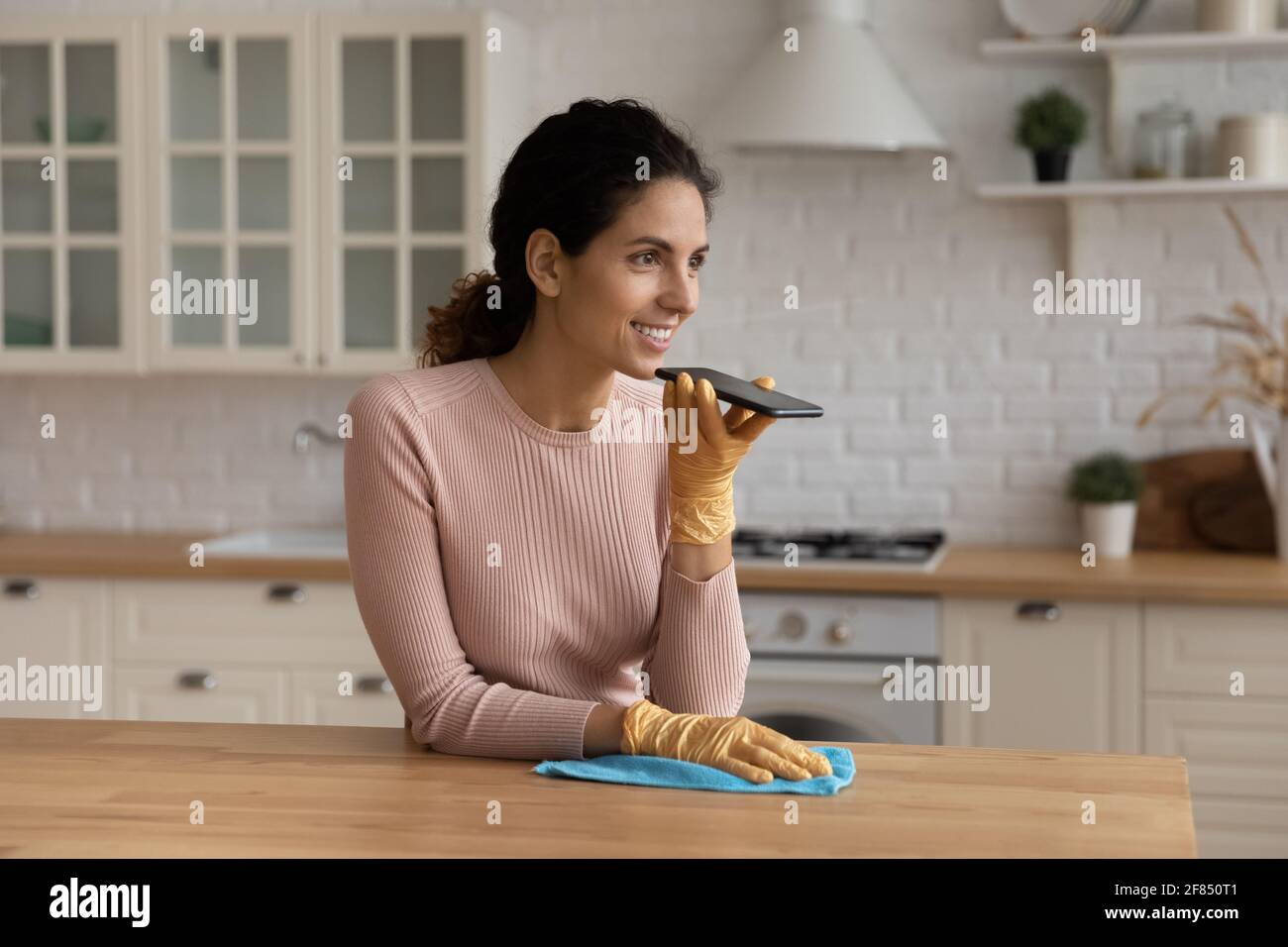 Junge lateinische Hausfrau Aufräumen Küche diktieren Nachricht am Telefon Stockfoto
