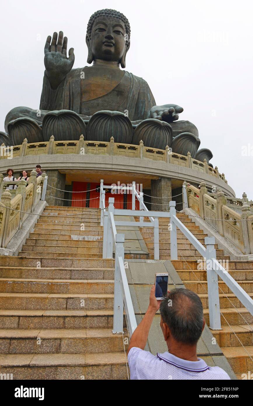 Ein Mann macht ein Foto vom Tian Tan buddha, während er über die Besucher wacht, die die Stufen bei Ngongping auf der Insel Lantau, Hongkong, China, klettern Stockfoto