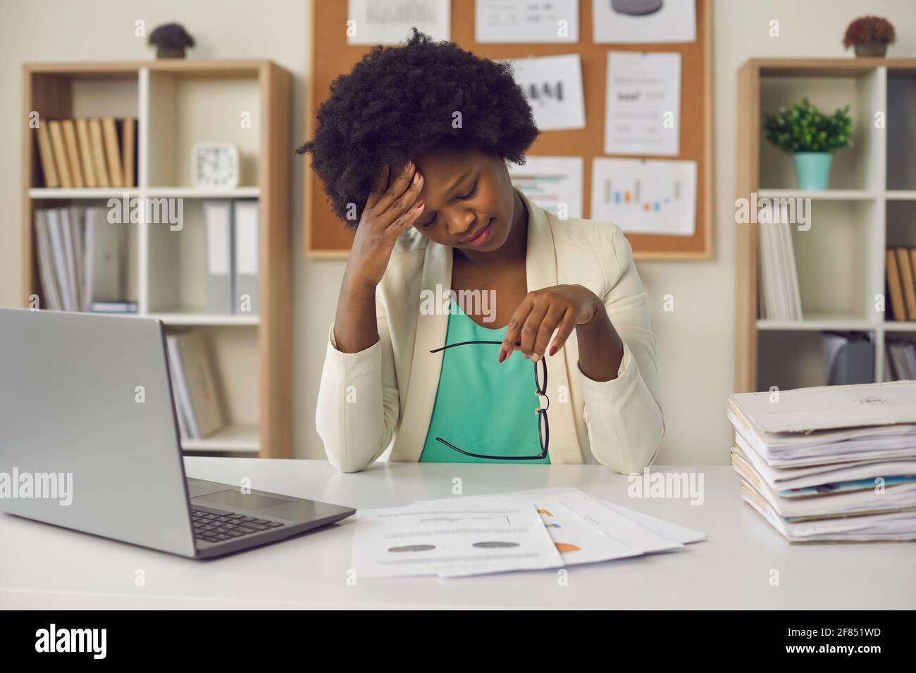 Müde afroamerikanische Geschäftsfrau, die unter Kopfschmerzen leidet, sitzt im Büro Tabelle Stockfoto