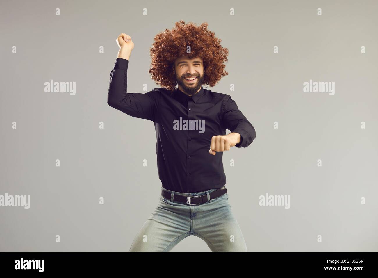 Glücklicher Kerl mit verrückten lustigen lockigen Haaren, die im gangnam-Stil tanzen Auf grauem Studiohintergrund Stockfoto