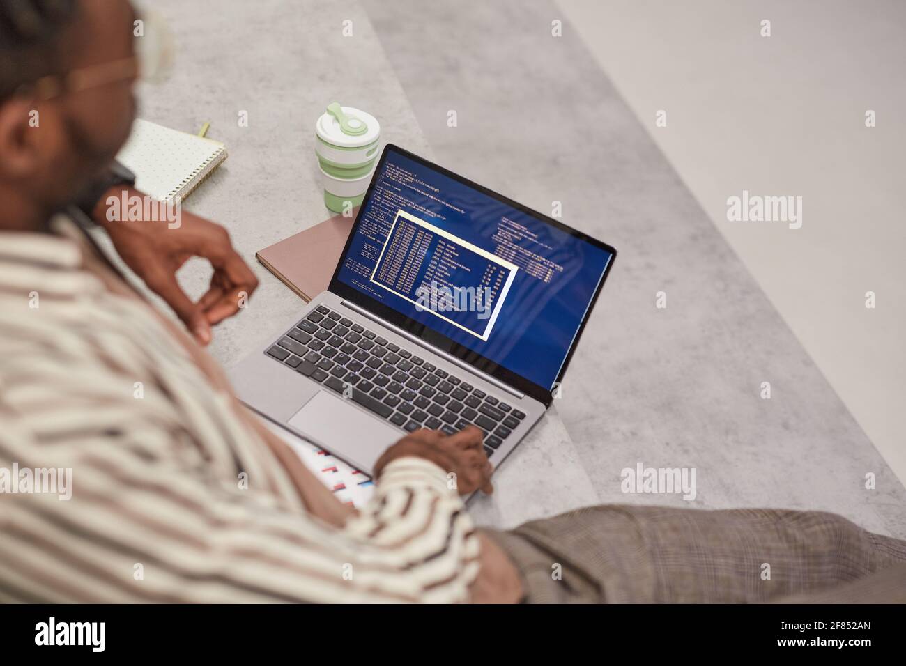 Blick auf den jungen afroamerikanischen Mann mit Laptop und IT-Code auf dem Bildschirm, während er im College studiert oder freiberuflich arbeitet, Kopierraum Stockfoto