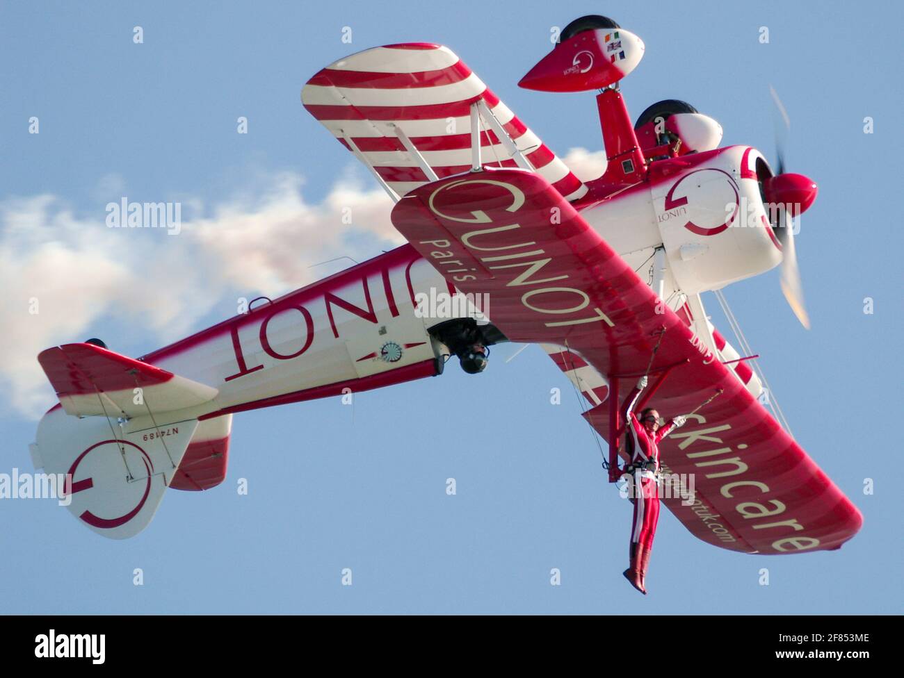 Sarah Tanner, Wing Walker mit Aerosuperbatics Wing Walking Team, das von Guinot hängt, sponserte Boeing Stearman Doppeldecker während des invertierten Stunts. Mutiger Akt Stockfoto