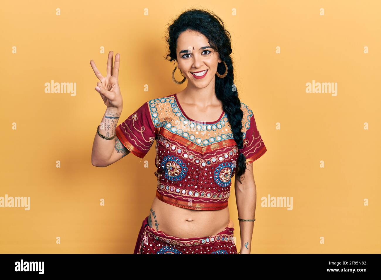 Junge Frau in Bindi- und bollywood-Kleidung zeigt und zeigt mit den Fingern Nummer drei auf, während sie selbstbewusst und glücklich lächelt. Stockfoto