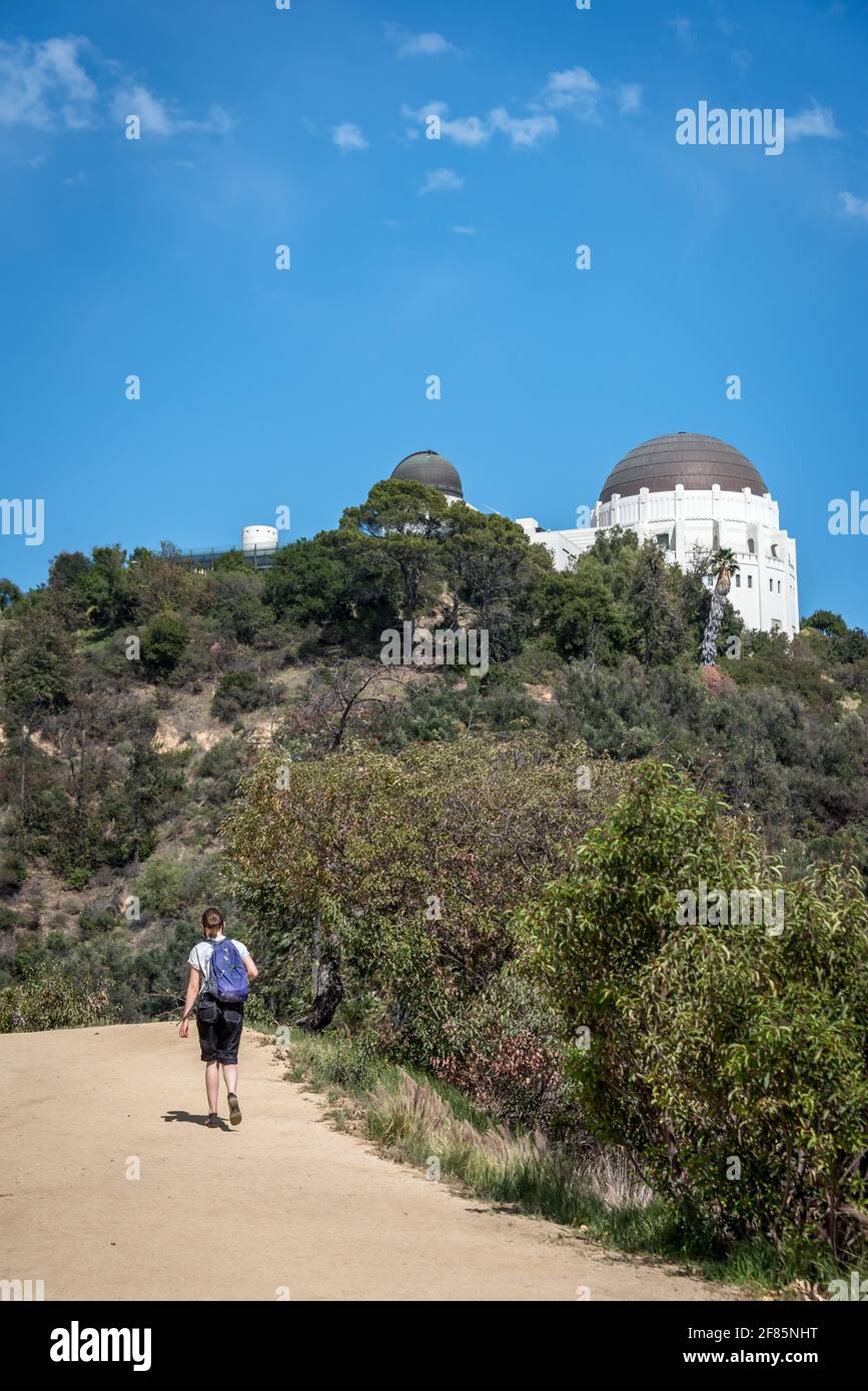Eine junge Frau wandert an einem schönen Tag auf dem Griffith Park West Observatory Trail mit dem Griffith Observatory oben, viel Platz für soziale Distanzierungen. Stockfoto