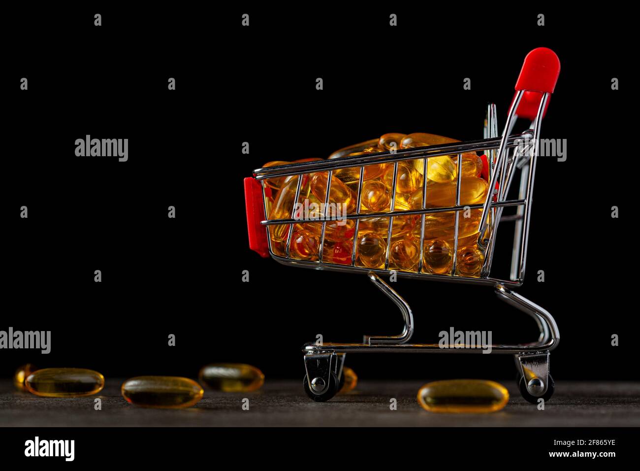 Dunkles Hintergrundbild mit einem Spielzeugwagen, der mit Omega-3-Fischölpillen gefüllt ist. Ein Konzept für den Kauf von rezeptfreien Nahrungsergänzungsmitteln Stockfoto