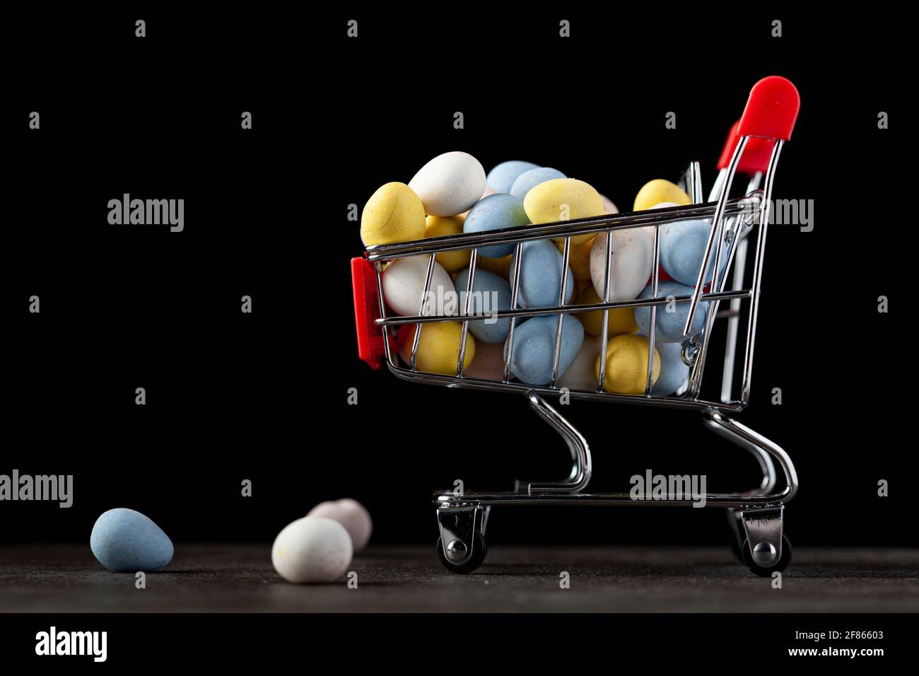 Dunkles Hintergrundbild mit einem Spielzeug-Warenkorb gefüllt mit Knusprig-zuckerbeschichtetes Schokoladenei EIN Konzeptbild für den Urlaub Shopping für weihnachten oder Osten Stockfoto