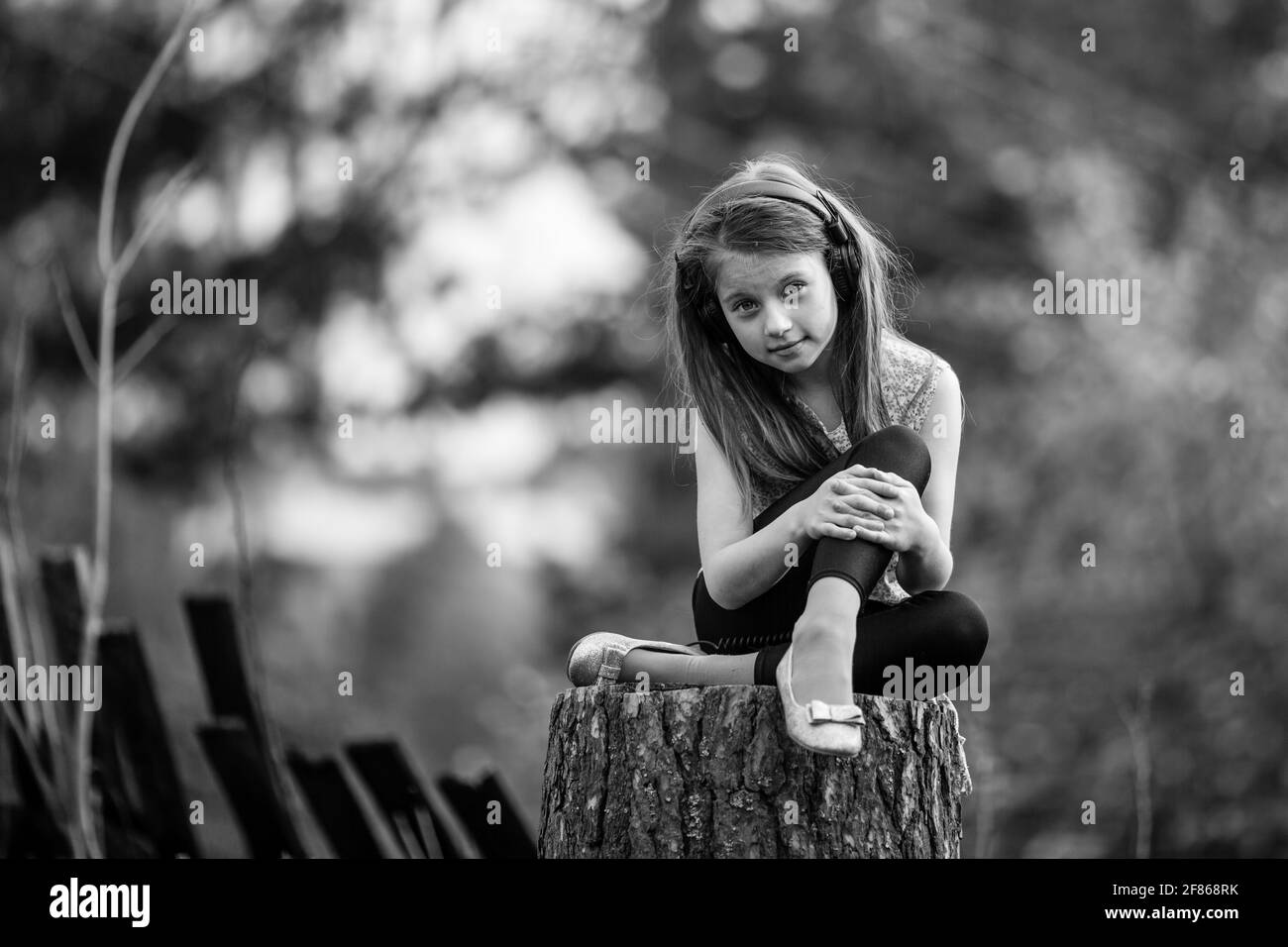 Kleines Mädchen, das auf einem Stumpf im Dorf sitzt. Schwarzweiß-Foto. Stockfoto