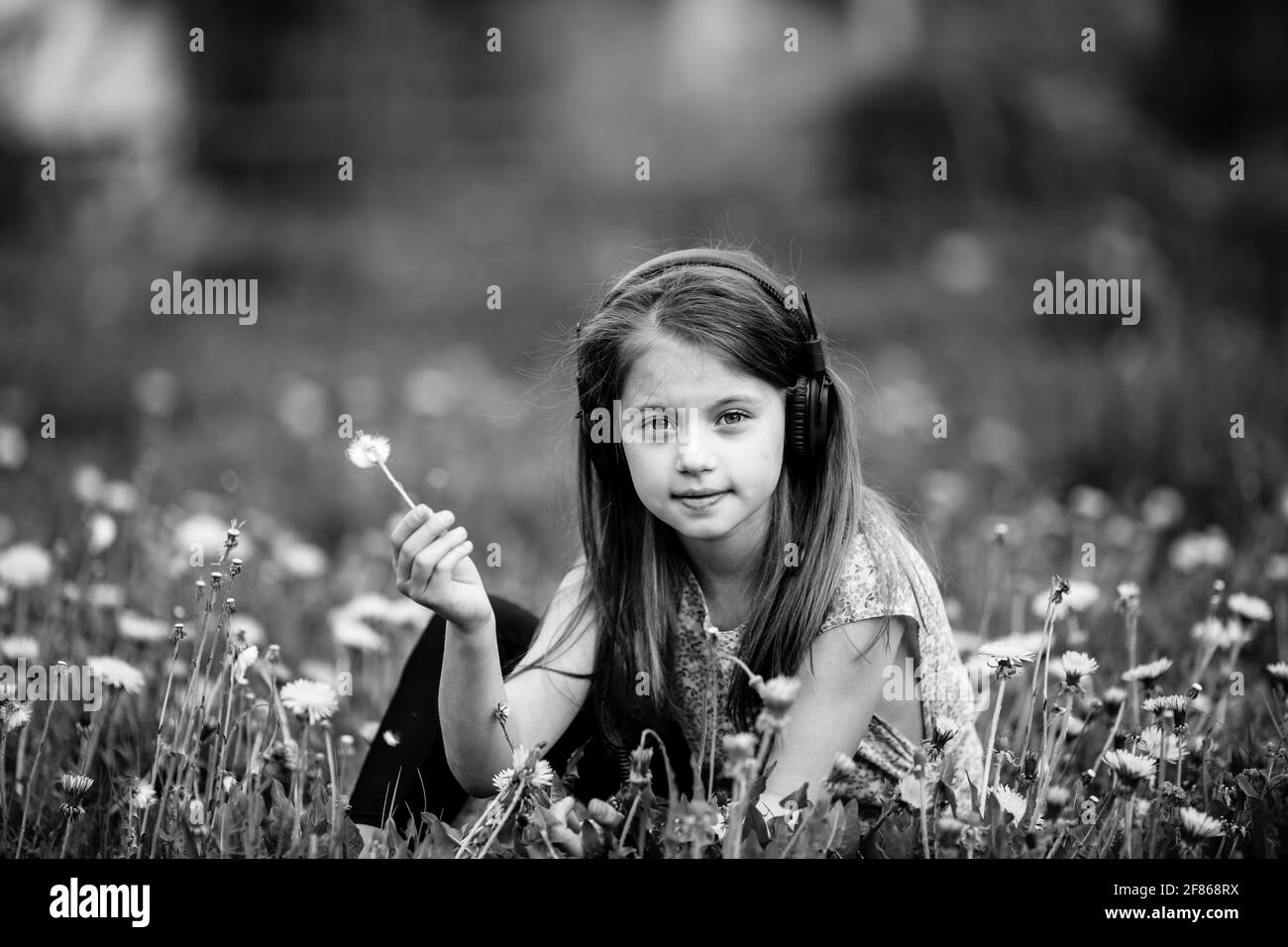 Kleines Mädchen, das auf dem Gras im Park sitzt. Schwarzweiß-Foto. Stockfoto