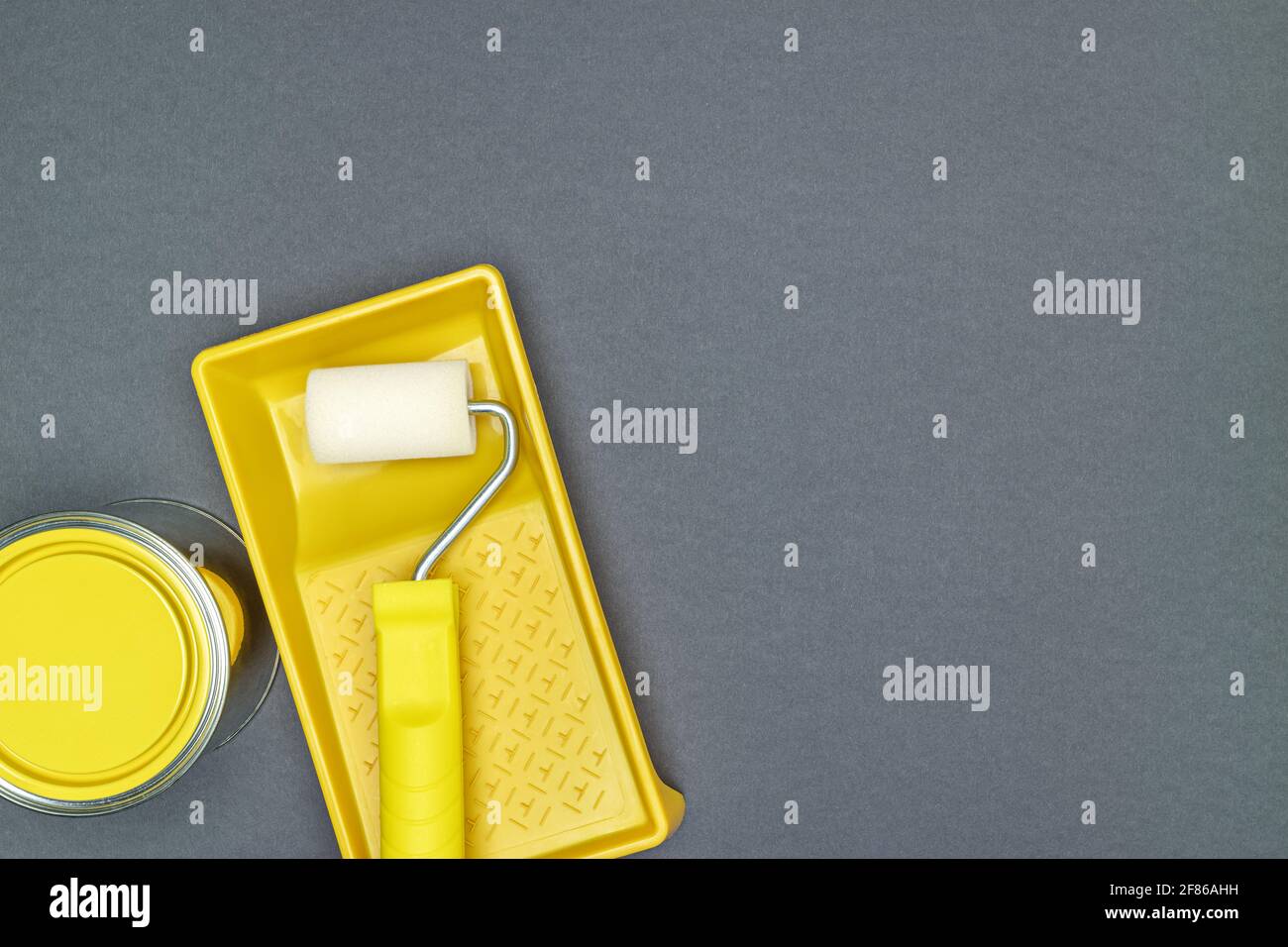 Gelbe Farbrolle in Farbtablett mit Dose gelber Farbe für Hausrenovierungen. Draufsicht auf grauem Hintergrund. Stockfoto