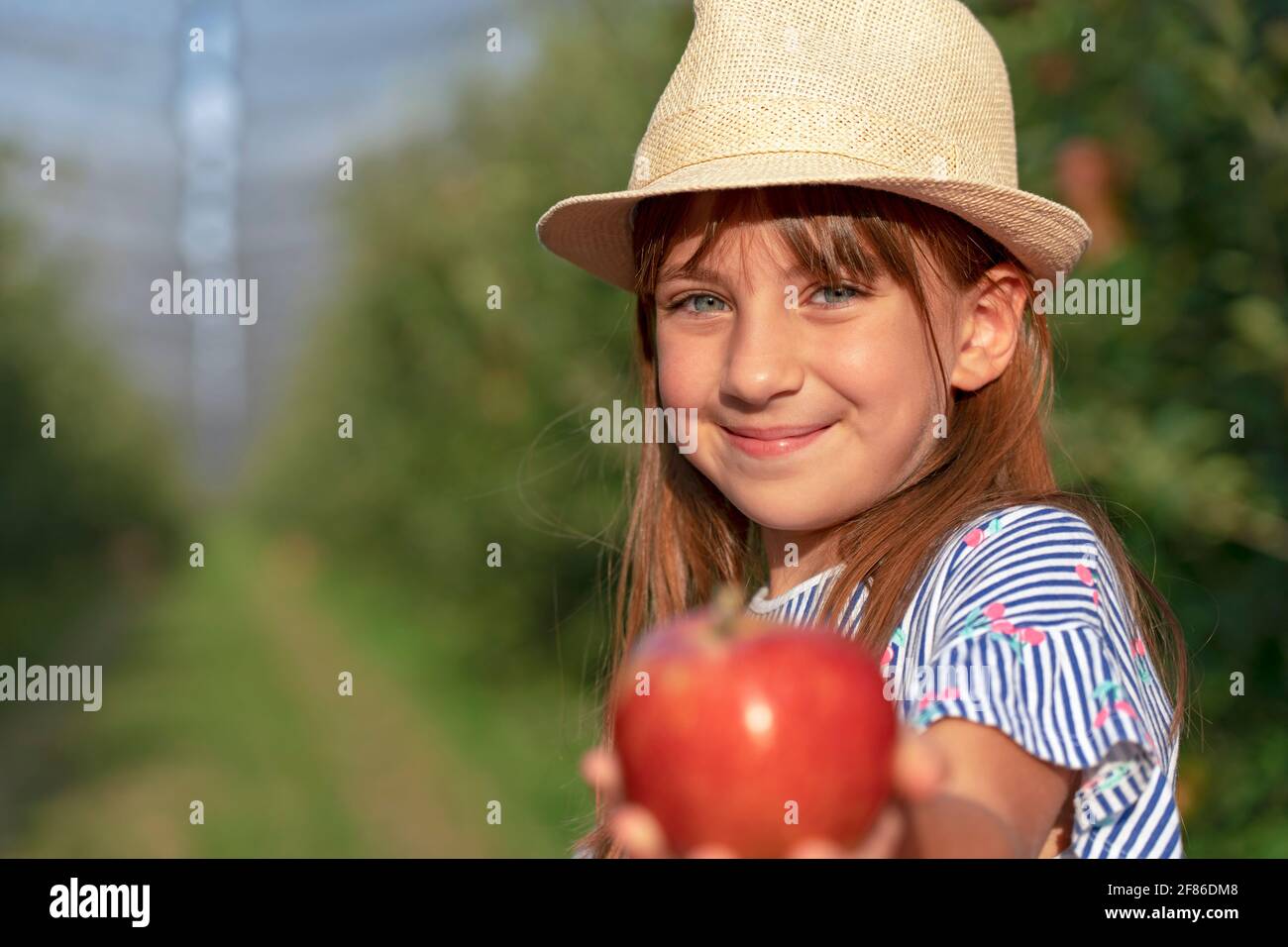 Porträt eines lächelnden kleinen Mädchens mit blauen Augen in einem Obstgarten. Konzept Für Gesunde Ernährung. Nahaufnahme Gesicht Aufnahme von niedlichen Mädchen mit Hut. Stockfoto