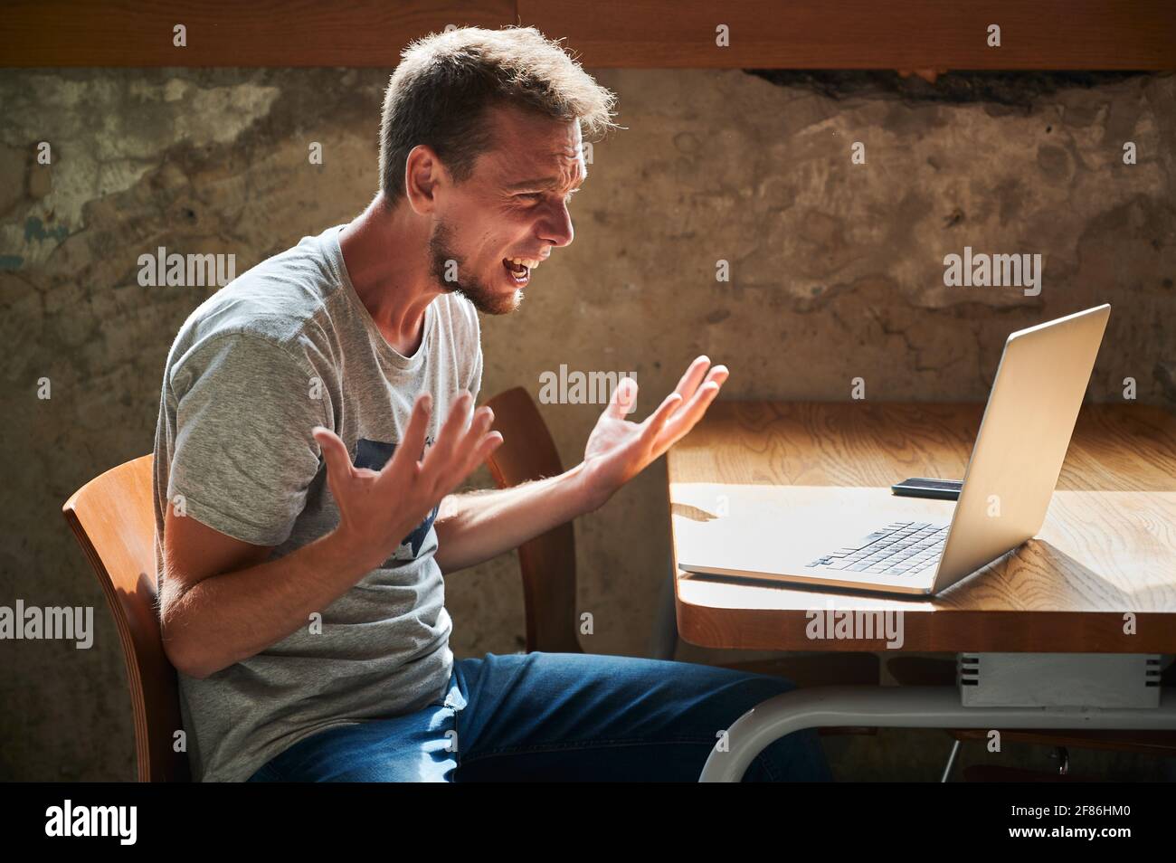 Seitenansicht eines verärgerten jungen Mannes, der mit einem Laptop arbeitet oder studiert. Konzept der verschiedenen Emotionen während der Arbeit im Café. Stockfoto
