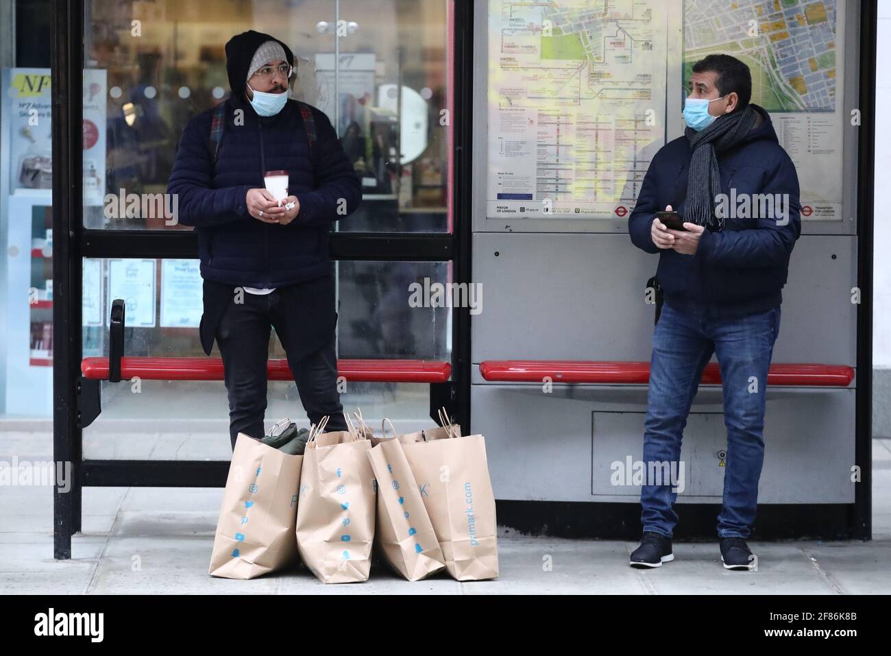 Zwei Männer stehen an einer Bushaltestelle in der Oxford Street, London, neben ihren Primark-Einkaufstaschen, nachdem das Geschäft am frühen Morgen wieder eröffnet wurde und die Sperrbeschränkungen in England weiter gelockert wurden. Bilddatum: Montag, 12. April 2021. Stockfoto