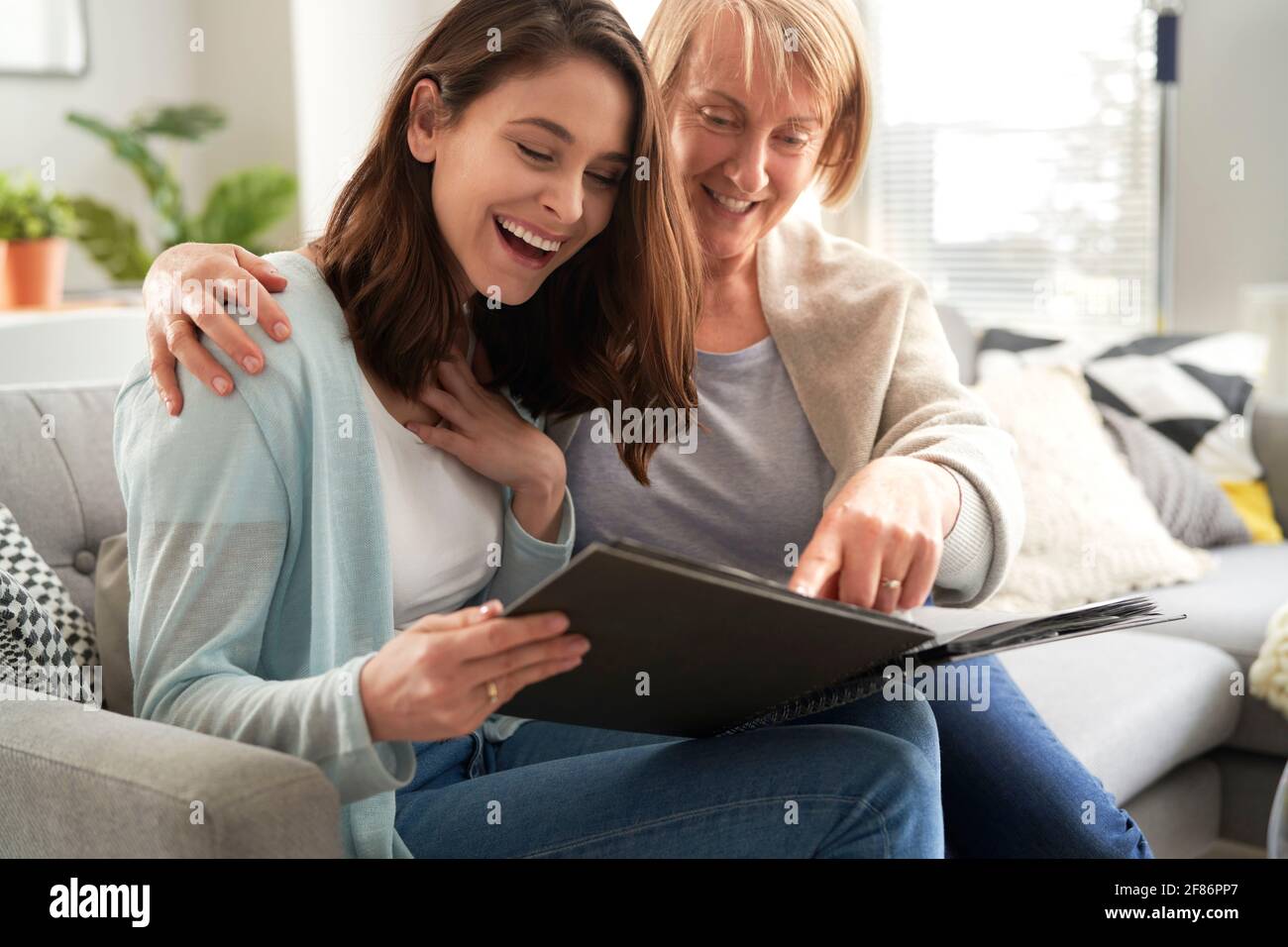 Glückliche Tochter und ältere Mutter suchen Fotoalbum zusammen Stockfoto
