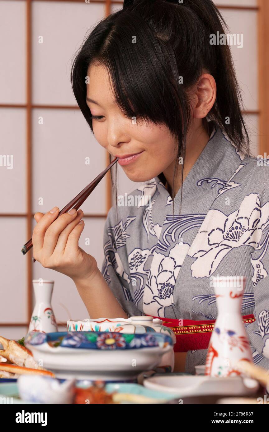 Junge Frau im Kimono, die traditionelle japanische Mahlzeit mit Essstäbchen isst Stockfoto