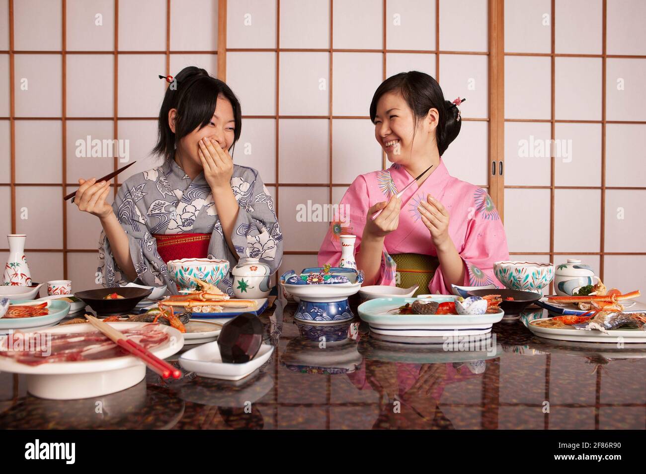 Glückliche junge Frauen in Kimonos essen im Restaurant zu Abend Stockfoto